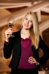 Beautiful young blond woman drinks wine in wine cellar
