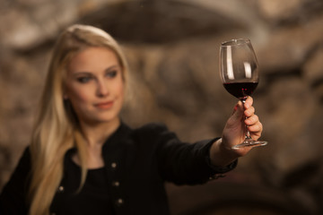 Beautiful young blond woman drinks wine in wine cellar