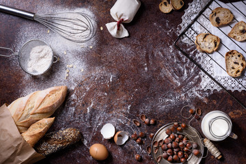 Bakery background, baking ingredients over rustic kitchen countertop. Baked cookies with hazelnuts, rye bread, milk and eggs. Top view, copy space.