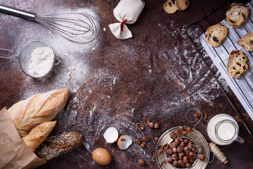 Bakery produce - bread, baguette, cookies over rustic background. Baking ingredients - flour, nuts, eggs, milk. Top view, copy space.