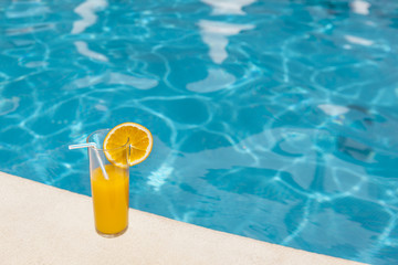 Glass of orange juice with orange slice on the edge of swimming pool