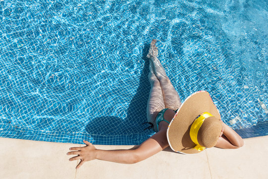 Tanned woman in hat relaxing on swimming pool