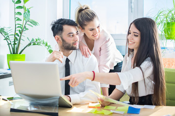 Obraz premium Young businesswoman showing something on laptop to her colleagues in the office.