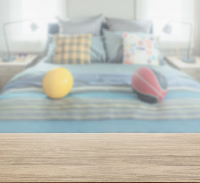 wooden table top with blur of bedroom with decorative pillow and football on bed