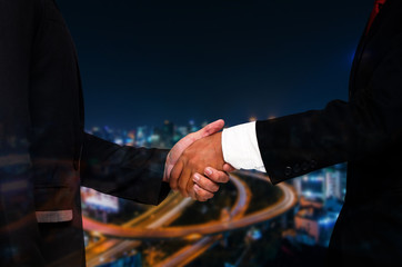 Double exposure of businessman handshake, business concept, successful business meeting on blurred night city background, color tone effect.