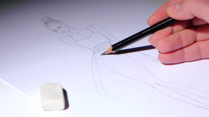 Designer creates fashion dress sketch, sitting at a white table. Close up
