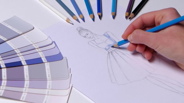 Designer dress decorates a sketch in blue, on a table cloth samples lie. Close up