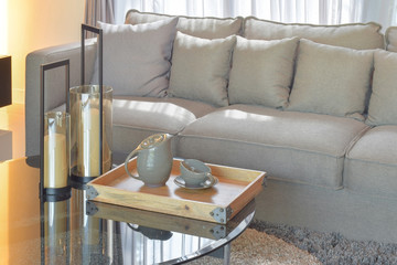 Wooden tray with pottery tea set and candles on glass top table next to sofa in the living room