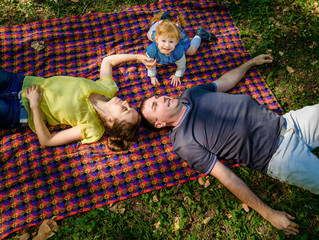top view of young happy family of three persons. Father, mother and daughter lying on plaid and having fun in the park