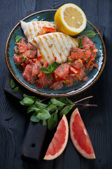 Grilled squid with grapefruit and mint salad on a black wooden background, studio shot
