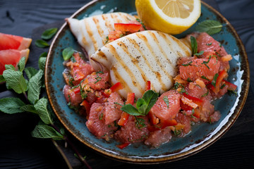 Glass plate with grilled squids and fresh grapefruit salad, closeup, studio shot
