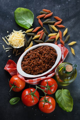 Bowl with freshly made bolognese sauce, raw penne pasta and other cooking ingredients, top view