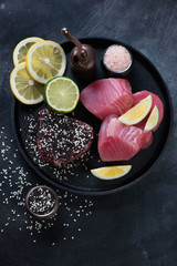 Frying pan with fresh uncooked tuna steaks, sesame seeds, pink salt, lemon and lime, view from above