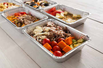 Healthy food take away in foil boxes on wood background