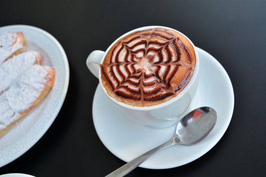 Cup of delicious foamy cappuccino with dessert on a black background.   