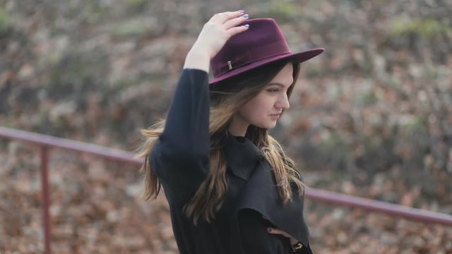 Beautiful young girl walks down in the park, long hair, autumn coat, holding her hat, side view, slow mo stedicam shot