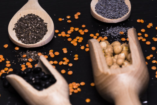Chia and poppy seeds, red and black lentils and chickpeas with wooden spoons on black background
