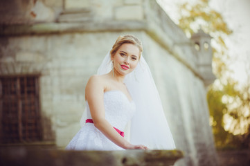 Beautiful bride walking near old castle before wedding ceremony