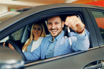 Young couple holding the keys of a new car - obrazy, fototapety, plakaty