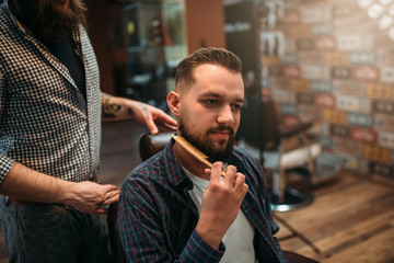 Male client combing his beard at the barbershop