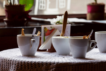 still life. White porcelain cups and a vase of flowers stand on a table with a white tablecloth in a brown cafe hall