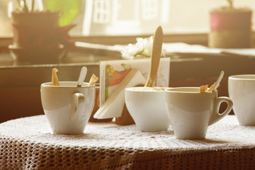 still life. White porcelain cups and a vase of flowers stand on a table with a white tablecloth in a brown cafe hall