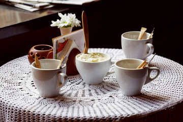 still life. White porcelain cups and a vase of flowers stand on a table with a white tablecloth in a brown cafe hall