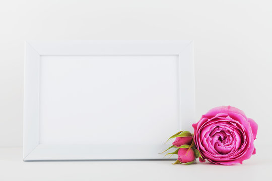 Mockup of picture frame decorated rose flower on white desk with clean space for text and design your blogging.