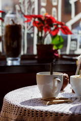 still life. White porcelain cups and a vase of flowers stand on a table with a white tablecloth in a brown cafe hall