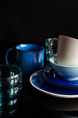 Obraz na płótnie Canvas Set of dishes. blue cups, glass and plates on the dark background. vertical