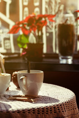 still life. White porcelain cups and a vase of flowers stand on a table with a white tablecloth in a brown cafe hall