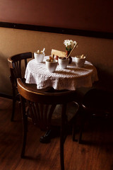 still life. White porcelain cups and a vase of flowers stand on a table with a white tablecloth in a brown cafe hall