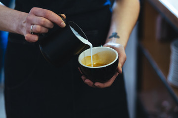 Close up shot of female barista creating espresso latte art by pouring steamed milk foam into a cup of espresso coffee.