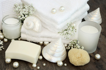 Fototapeta na wymiar Body Care Cleansing Products. With white bathroom accessories, moisturising cream, soap, white flannels, natural sponge, candle, mother of pearl shells and pearls.