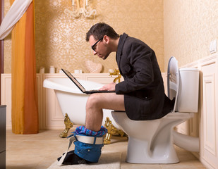 Man in glasses with laptop sitting on toilet bowl