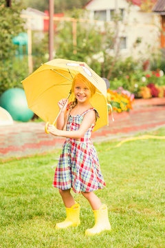 Happy girl with an umbrella in rubber boots after a rain on a summer day in the park