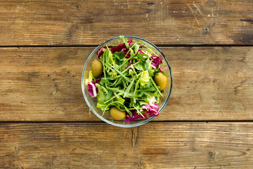 Green salad with olives in glass bowl.