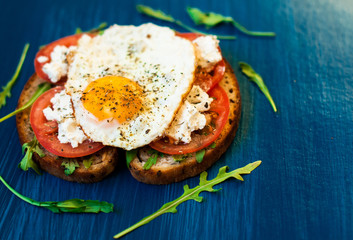 Sandwich with feta cheese and tomatoes, fried eggs for breakfast. Dark background, top view