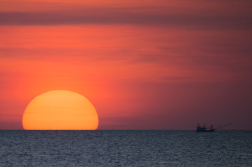Big sun and a fisherman boat at sunset in Phuket - Thailand