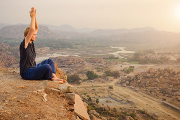 Naklejka na ściany i meble Young man practicing yoga at mountain cliff on sunrise