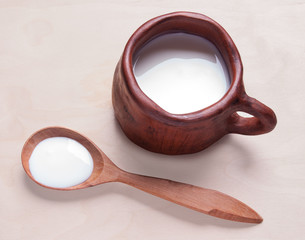 Milk  in a large clay mug.  Sour cream in wooden spoon isolated. sauce, yogurt, kefir, milk. Country breakfast.