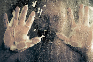 stressed man taking a shower standing under flowing water and holding his head in shower cabin behind transparent misted glass door in the bathroom