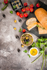 Homemade traditional Italian appetizer tapenade from green and black olives, white ciabatta, fragrant herbs and oil, fresh tomatoes. On a concrete gray table, copy space top view