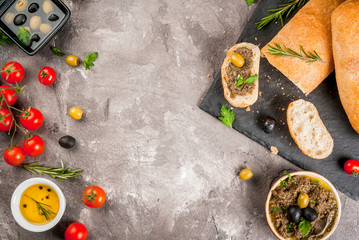 Homemade traditional Italian appetizer tapenade from green and black olives, white ciabatta, fragrant herbs and oil, fresh tomatoes. On a concrete gray table, copy space top view