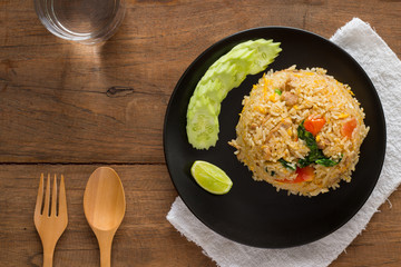Fried rice with cucumber on black circle plate on wooden table