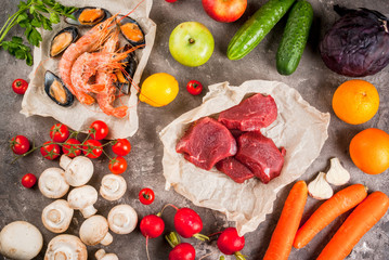 Selection of healthy dietary food products - raw beef, seafood, vegetables, fruits and greens. On a concrete gray table, top view 