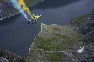 three basejumpers jumping from huge mountain in Norwegian fjord blue and yellow smoke