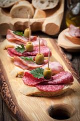 Tapas with sliced sausage, salami, olives and parsley.