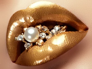 Kosmetik und Schminke. Nahaufnahme von goldenen künstlerischen Lippen. Glitzerndes Lippen-Make-up. Aufnahme eines schönen Mädchens mit goldenem Lippenstift und Glanz. Sexy und stilvolle Lippen. Perlen und Diamanten in ihrem Mund © looking2thesky