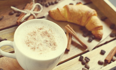 White cup of cappuccino and croissant on the wooden tray. Vintage style